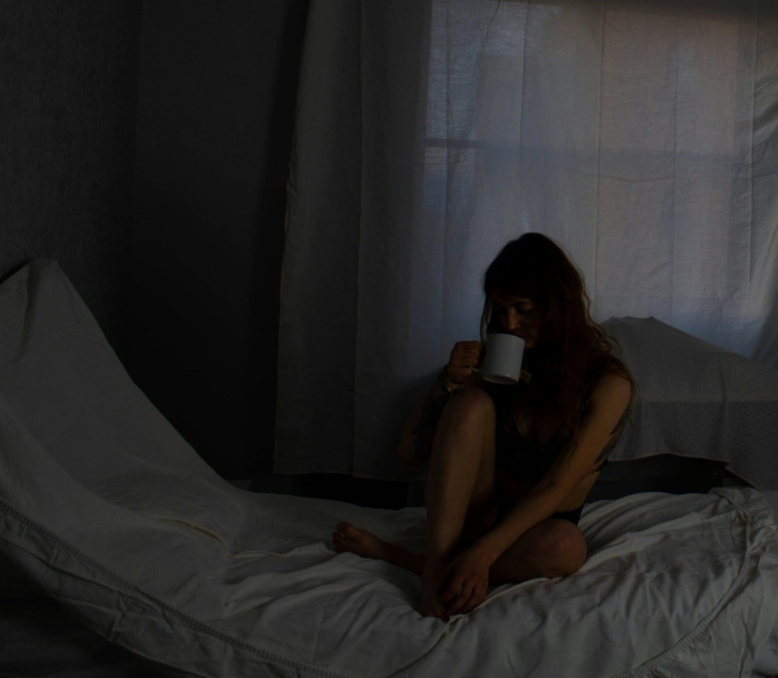 Person sitting on her bed while sipping tea on a quiet, sad day.
