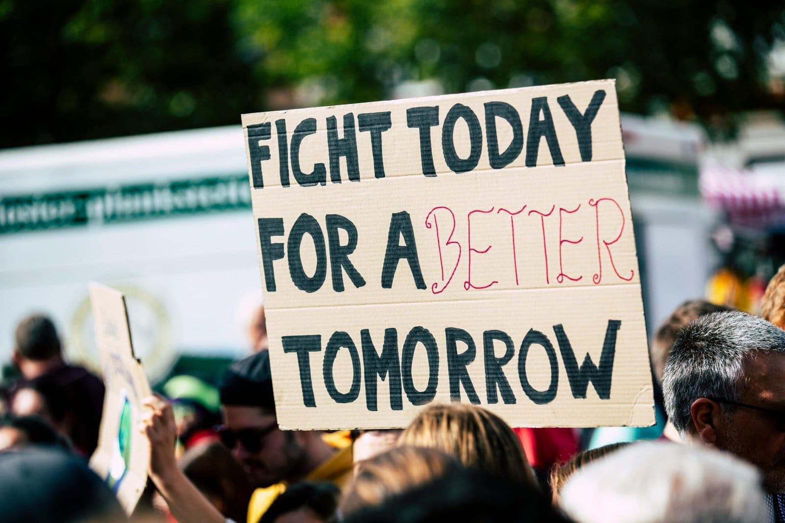 A close-up of a protestor holding a sign that reads 'FIGHT TODAY FOR A BETTER TOMORROW' in bold letters, emphasizing the call for action and change.