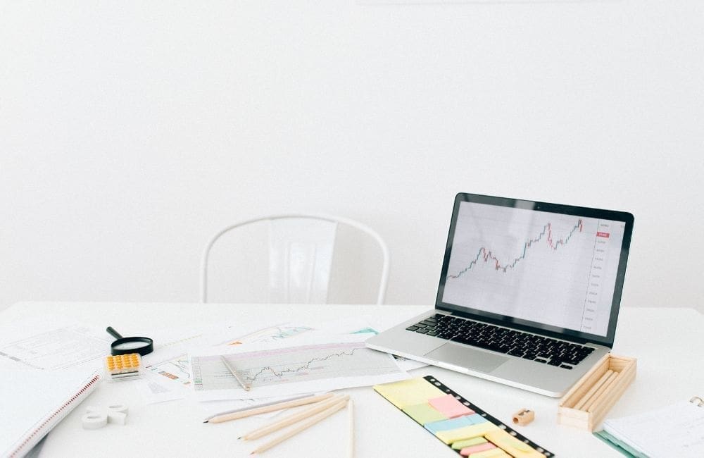 A clean workspace with a laptop displaying a financial graph, surrounded by pens, papers, and other office supplies.