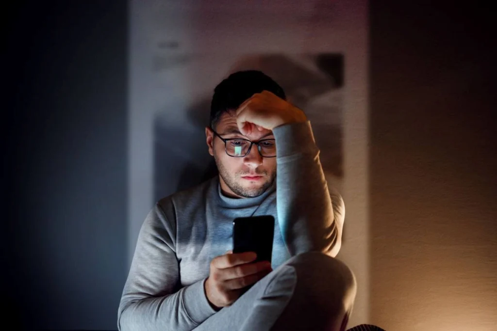 Young man scrolling on his phone, looking thoughtful and reflective.