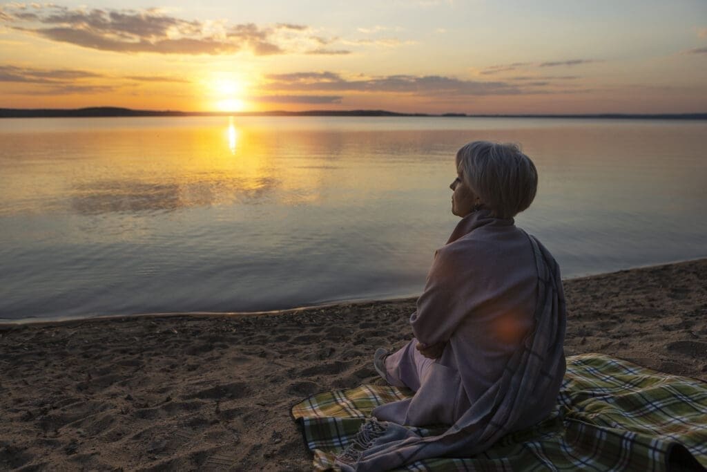 nature therapy by water, person sitting peacefully by a lake at sunrise