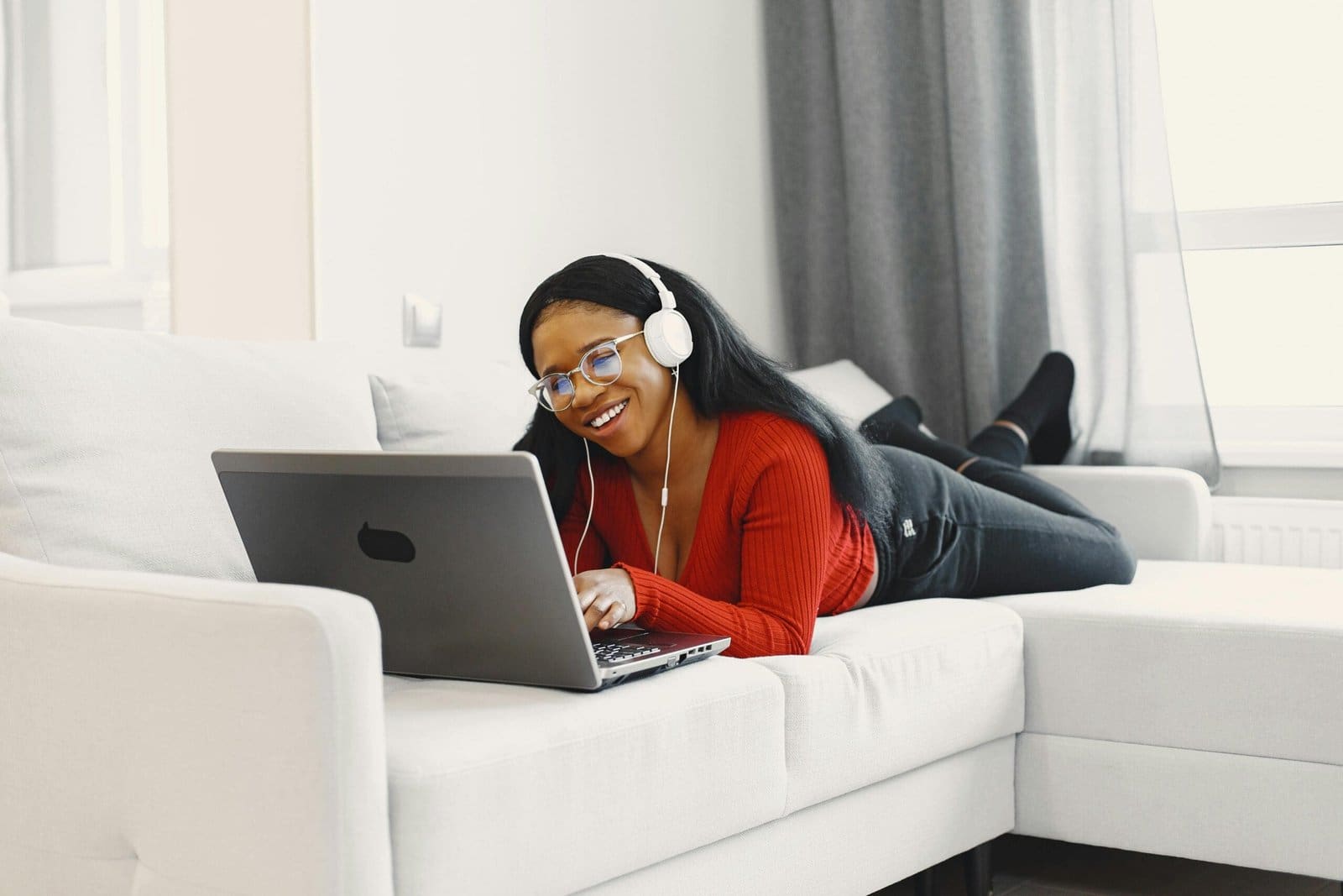 A content creator lying on a sofa, smiling while working on her laptop, reflecting healthy social habits and balanced work-life routine.