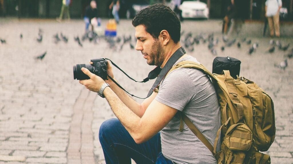 Man kneeling on one knee while holding a DSLR camera, filming a travel scene.