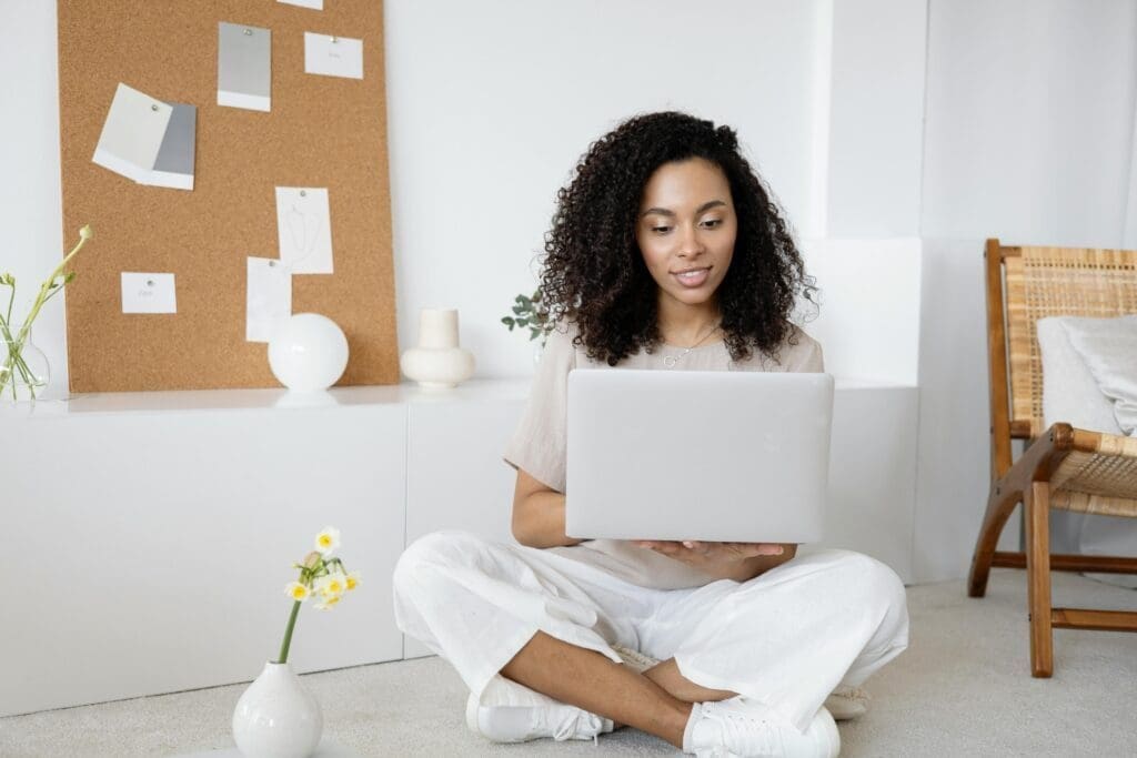 Woman sitting cross-legged on the floor using a laptop to plan her travel diary series.