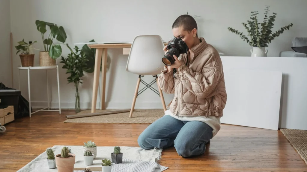 Hands holding a camera, photographing a minimalist flat-lay of indoor plants on a clean surface.