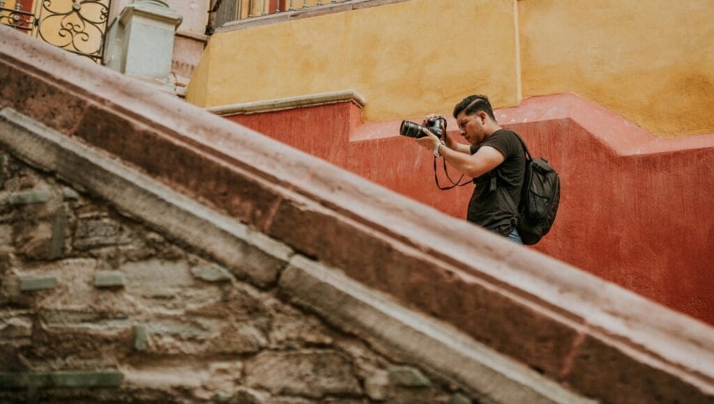 Traveler walking through a colorful city street with a camera, filming a silent city walk vlog at sunset.