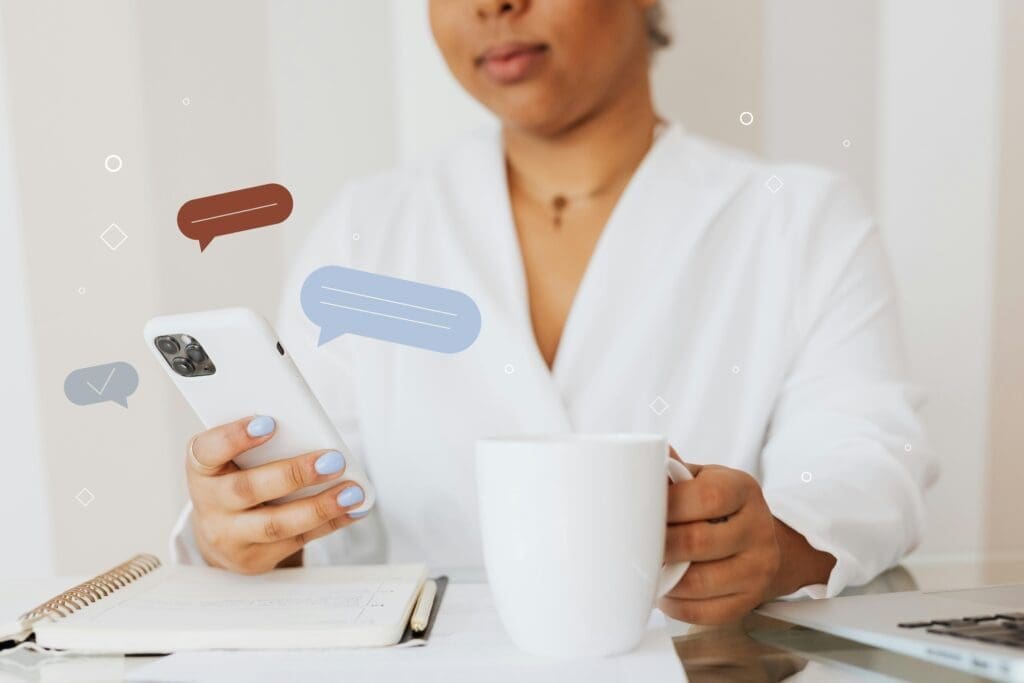 Hands holding a smartphone displaying social media icons, surrounded by coffee, notebook, and minimal props, representing privacy and creative faceless content.