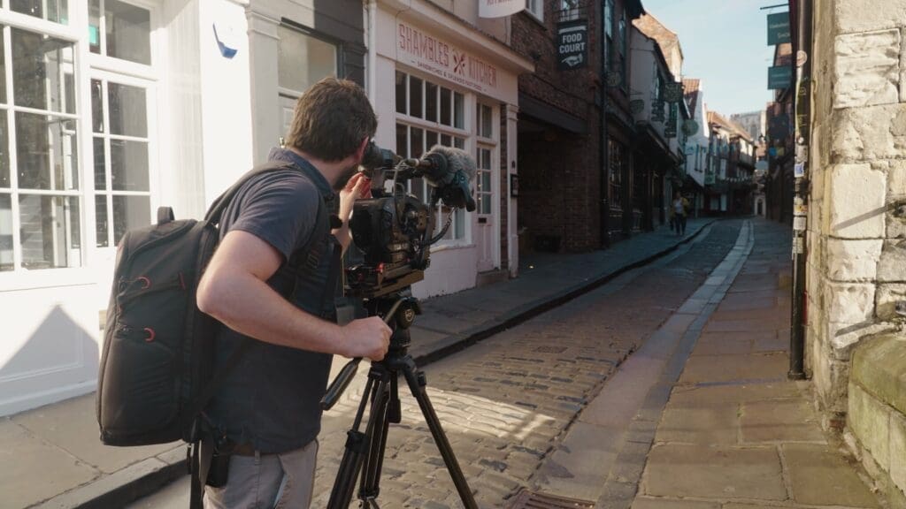 A cinematographer films a wide street scene with passing traffic, capturing everyday life from a distance.